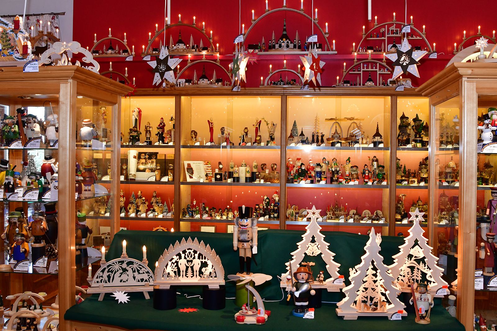 Ein Raum mit Holzregalen voller erzgebirgischer Weihnachtsdekoration Vorne stehen traditionelle Lichterbögen und im Hintergrund ist eine Wand mit roten und gelben Lichtern