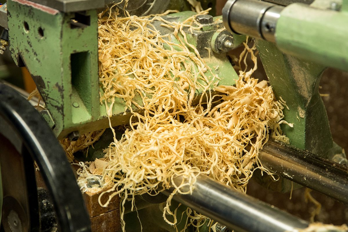 Nahaufnahme einer Drehbank mit gelben Holzspänen die aus dem bearbeiteten Holz fliegen grüner Metallrahmen und schwarze Teile sichtbar