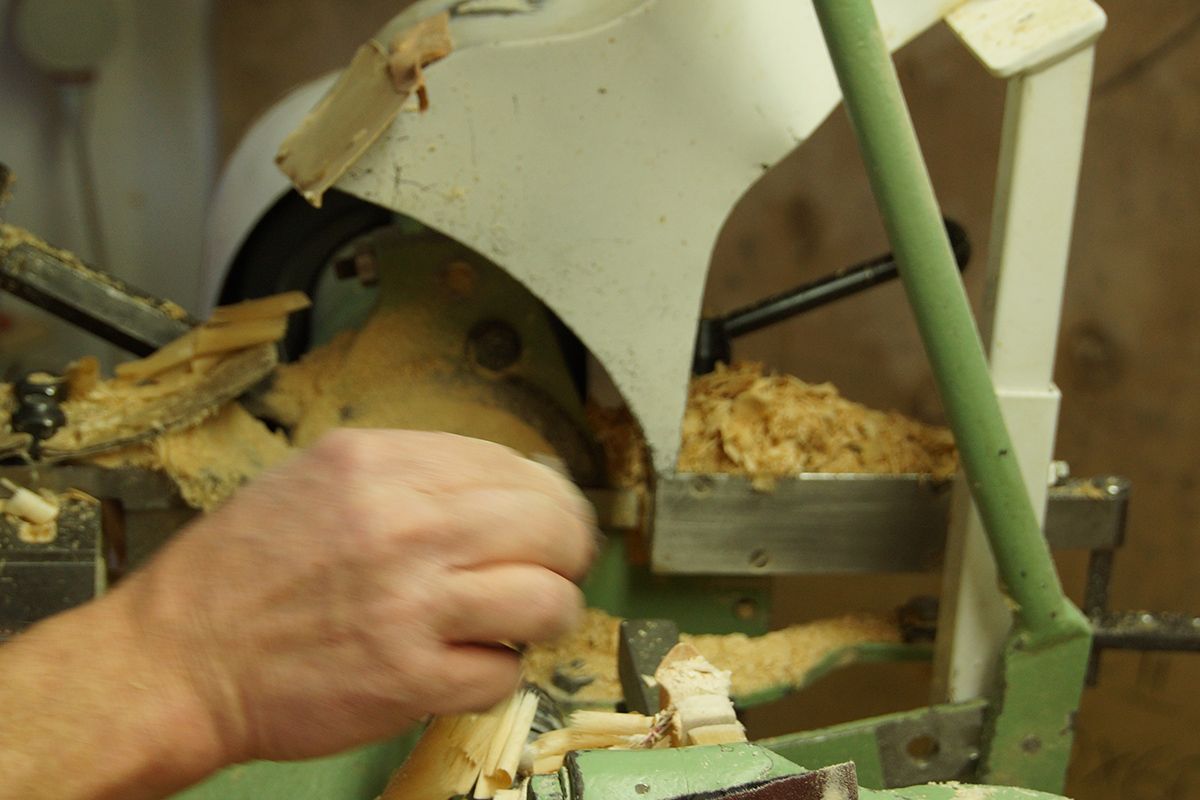 Eine Hand bearbeitet Holz an einer grünen Maschine mit Holzspänen die herausragen weißer Metallrahmen sichtbar